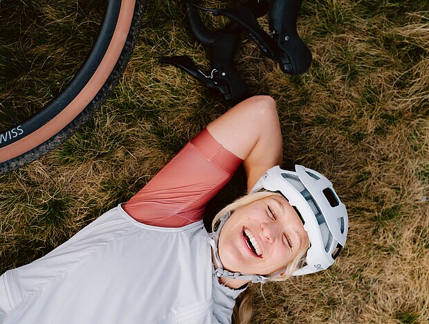 Frau liegt im Gras und genießt den moment, neben ihr liegt ihr Gravel-Bike