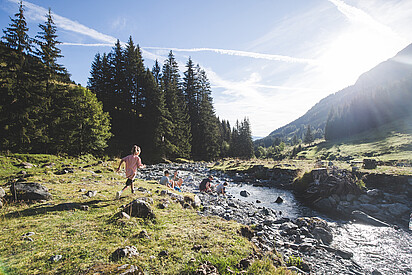Girl walking to the family towards the river bank, Saalbach Hinterglemm valley head